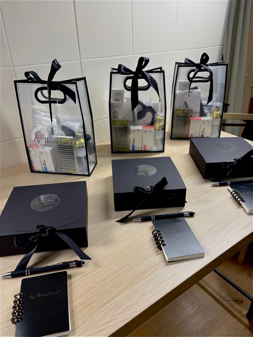 Tres kits de formación preparados en bolsas con el logotipo by MariaFinol, junto a cajas, libretas y bolígrafos de la marca